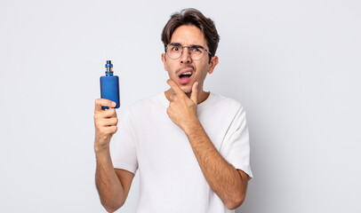 young hispanic man with mouth and eyes wide open and hand on chin. smoke vaporizer concept