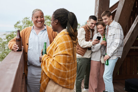 Diverse Group Young People Drinking Beer On Balcony During Party At Lake House