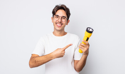 young hispanic man smiling cheerfully, feeling happy and pointing to the side. lantern concept