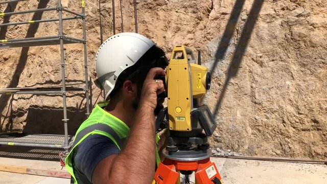 Geodetic or topographic works at construction site. Land surveyor doing a measurements on total station. Topographer looks to theodolite telescope