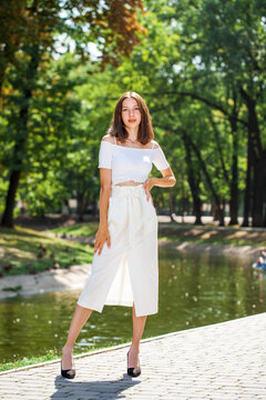 Young beautiful brunette girl in a white skirt posing in a summer park