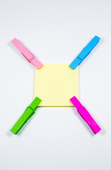 Blank yellow sticker with colorful wooden clothespins. Close up of note paper on white background. Copy space.