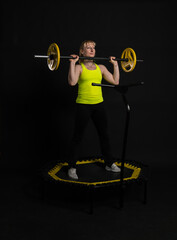 Naklejka na ściany i meble Girl on a fitness trampoline on a black background in a yellow t-shirt black gym jump, activity female movement, weight rebounder. Person white aerobics, physical muscle instructor enjoy