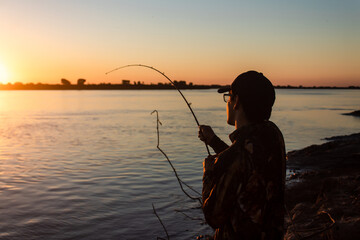 Young man pulling hard on his fishing rod to pull a fish out of the river.