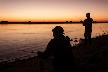 Friends fishing on the edge of the river at sunset.
