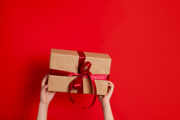Merry Christmas. Children's hands hold a gift box tied with red ribbon on a red background. A place for text.