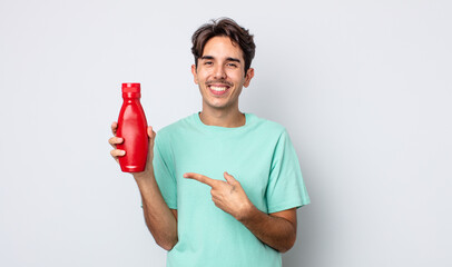 young hispanic man smiling cheerfully, feeling happy and pointing to the side. ketchup concept - obrazy, fototapety, plakaty