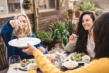 Happy friends having fun drinking and eating vegan food at patio restaurant - Focus on hand holding artichoke