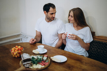 Couple in the kitchen is drinking coffee. A guy and a girl in white t-shirts