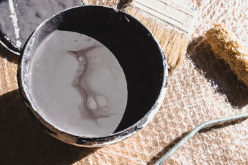 A bucket of paint, paint roller and paint brush lying on isolation material on ground