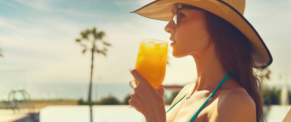 Side profile cropped panoramic view face beautiful woman, wear straw hat hold glass drinks orange...