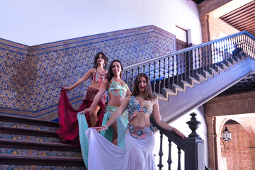 Three middle-aged Hispanic women in beautifully colored dresses with rhinestones to belly dance,...