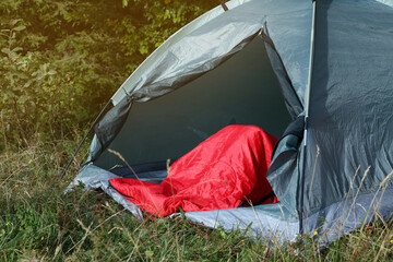 Red sleeping bag in camping tent on green grass outdoors