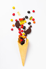 Wafer cone with sweets, marmalade, cookies and chocolate pills on a white background