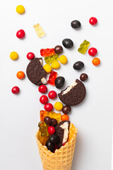 Wafer cone with sweets, marmalade, cookies and chocolate pills on a white background