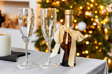 Festive Christmas background. Cozy home evening. Two glasses and a bottle of champagne on the background of a Christmas tree and bokeh of garlands