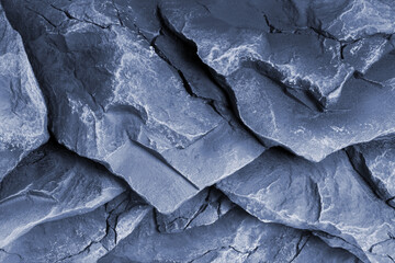 Embossed and rough dark stone or rock texture of mountains divided by huge cracks and layers.