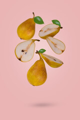 Creative food concept with fresh ripe whole and sliced pears flying in air isolated on a light pink background.