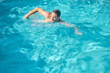 Fototapeta na wymiar A young man in sunglasses swimming in a pool