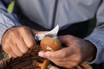 Man peeling mushroom with knife over basket, closeup