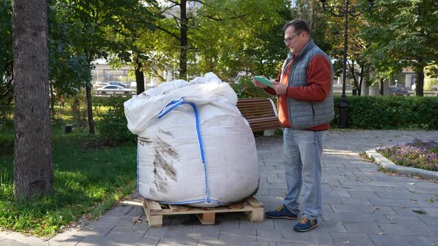 Man with a tablet checks the quality of the contents of a large white bag