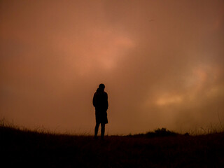 Silhouette of a camper watching the sunrise in the mist from top of 'Le Pouce' mountain located in Mauritius