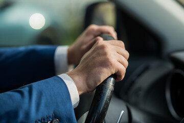 Close-up of a businessman holding a steering wheel of a car. Male hands in a blue suit on the...