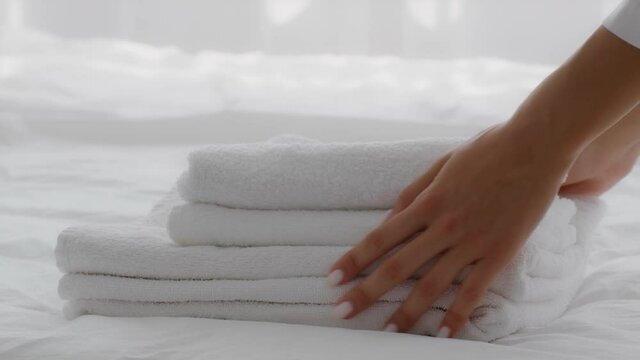 Female hands putting stack of fresh white bath towels on bed, closeup