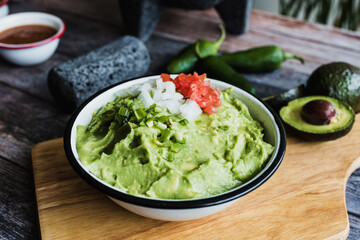 Bowl of Guacamole next to fresh ingredients on a wooden table in Mexico	
