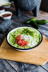 Bowl of Guacamole next to fresh ingredients on a wooden table in Mexico	