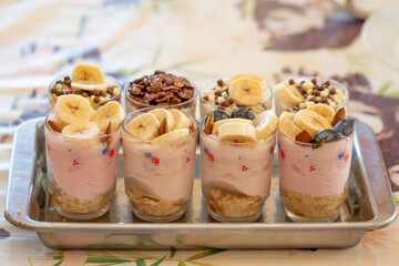 Yogurt dessert with different fruits, crushed cookie and chocolate, presented in crystal glasses decorated with floral elements.