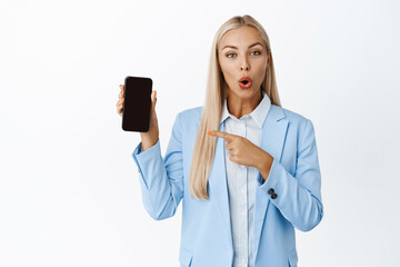 Amazed businesswoman pointing at mobile phone screen, showing interesting concept on smartphone,...