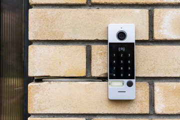 an intercom on the door of a private house, an intercom panel with a video camera on a brick beige fence post - obrazy, fototapety, plakaty