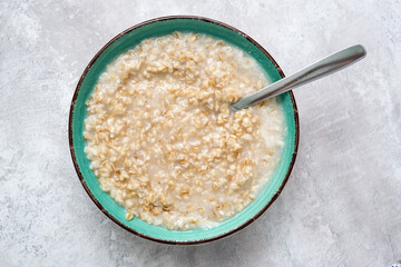A green bowl of cooked oats porridge with a spoon close up, healthy breakfast and dieting product close up
