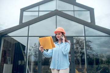 Attentive woman with document talking by smartphone