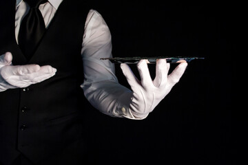 Portrait of Butler or Waiter in Black Vest and White Gloves Holding Silver Serving Tray on Black Background. Copy Space for Service Industry and Professional Hospitality.