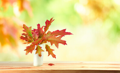 Naklejka na ściany i meble Red autumn leaves in small vase on wooden table against blurred natural background