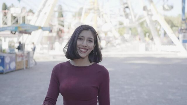 Nice-looking multi-race brunette beautiful elegant young woman looking into camera. Female looking happy and excited , walking to amusement park fun fair background. Funny concept.