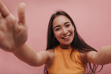 Close-up of beautiful young lady of exotic appearance playing with camera in studio. Dark-haired woman laughs at bright background in summer yellow top. Mood, lifestyle, concept.