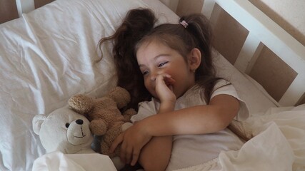 little cute girl is going to go to bed. indulges in, does not want to sleep. naughty. Cute little girl sleeping with teddy bear in bed