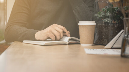 A man's hand with a pen lies on a notebook. Pause while writing in a notebook for coffee.