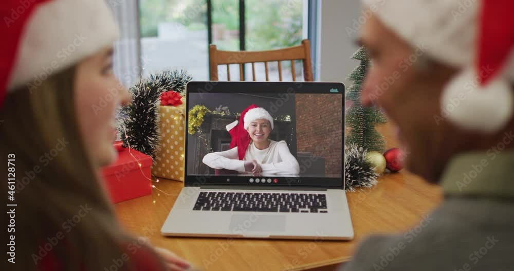 Sticker Rear view of caucasian couple wearing santa hats having a videocall on laptop during christmas