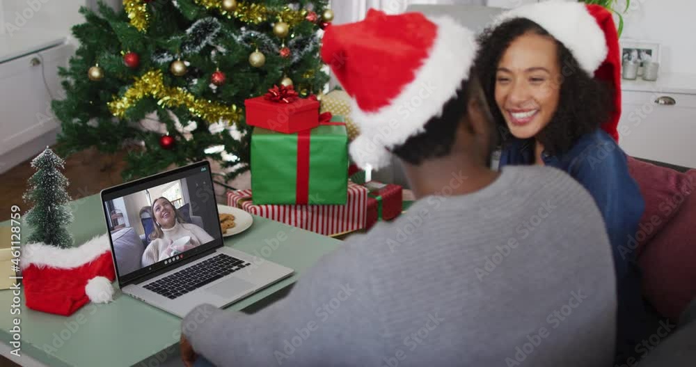 Poster African american couple wearing santa hats having a videocall on laptop at home during christmas