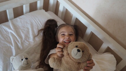 little cute girl is going to go to bed. indulges in, does not want to sleep. naughty. Cute little girl sleeping with teddy bear in bed