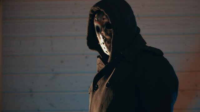 A terrible villain killer in a dark room at night goes to the corridor. Frightening character in a carnival costume with a long black cloak, a sinister mask and a knife in his hands. Cinematic concept