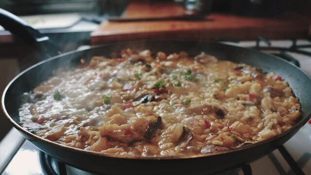 Cooking chicken risotto with onion and parsley on a kitchen stove in daylight