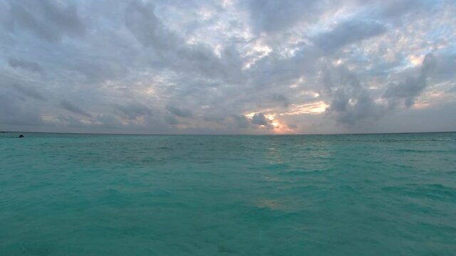 The setting sun hid behind gloomy leaden clouds and cast glare on the turquoise waves
