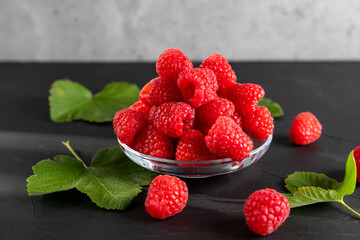 A glass bowl with scarlet ripe raspberries on the dark background.