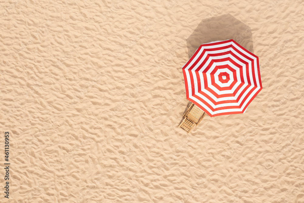 Wall mural Striped beach umbrella near wooden sunbed on sandy coast, aerial view. Space for text