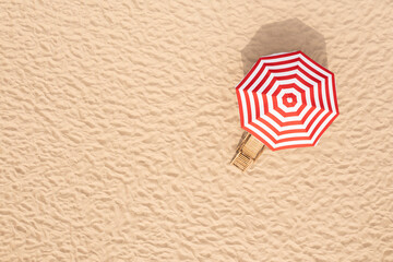 Striped beach umbrella near wooden sunbed on sandy coast, aerial view. Space for text